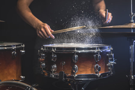 A male drummer plays snare drum with drumsticks in a dark room.の写真素材