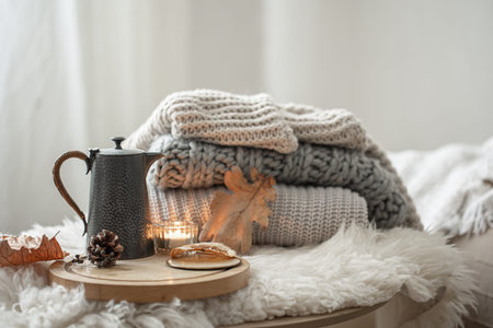 Home still life with knitted sweaters and teapot of tea on blurred background.