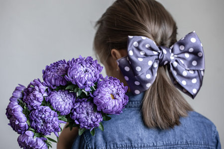 Little girl with a beautiful bow on her hair holds a bouquet of blue chrysanthemums, back view.