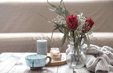 Cup, candles, vase with protea flowers and a knitted element in the room on a blurred background.の写真素材