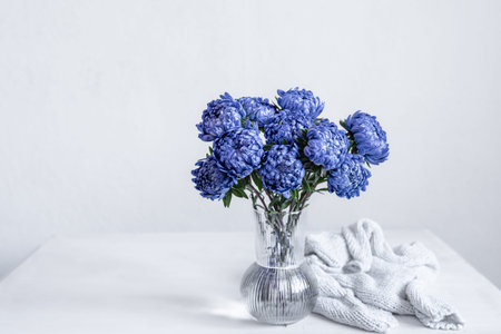 A bouquet of blue chrysanthemums in a glass vase and a knitted element on a white background, copy space.の写真素材
