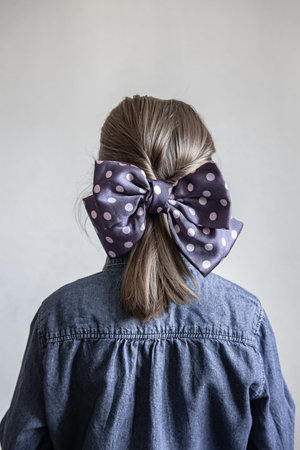 Back view, portrait of a schoolgirl with a beautiful blue polka dot bow on her hair.