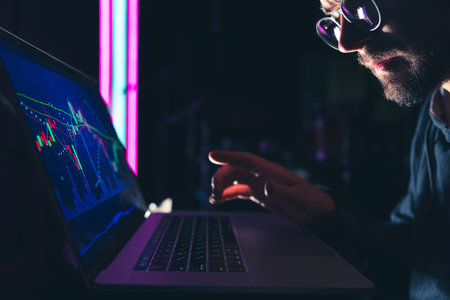 A man stares intently at a computer screen late at night. Concept of a digital diagram, graph interface, virtual screen, technical price indicator, trading online, global market, a broker at work.の写真素材