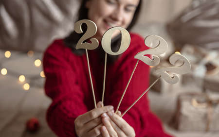 Girl in a red sweater holds wooden numbers 2022 on sticks, blurred background with bokeh.の写真素材