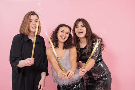 Beautiful cheerful festively dressed girls on pink background with candle fireworks, new year party conceptの写真素材