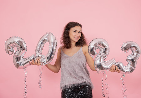 Beautiful brunette girl with curly hair and festive clothes posing on a pink background with...