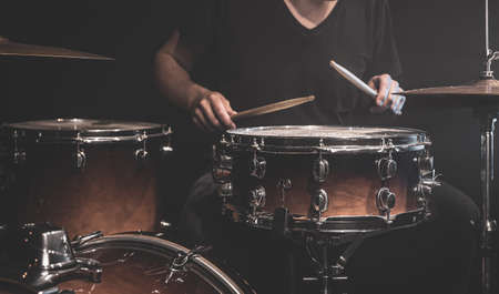 A musician in a black T-shirt plays drums with sticks on stage.の写真素材