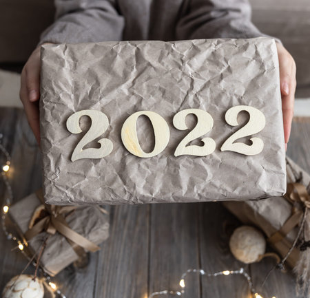 Christmas gift box with wooden numbers 2022 in female hands, close-up.