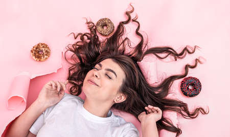 Cute young brunette woman on a paper pink background with donuts, top view.の写真素材
