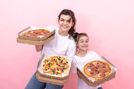 Cheerful adult girl and her little sister with pizza in boxes for delivery on a pink background.の写真素材