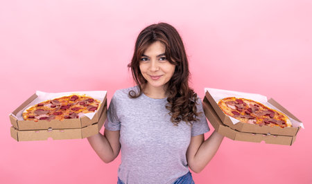 Nice brunette girl holding pizza in boxes for delivery on a pink background.の写真素材