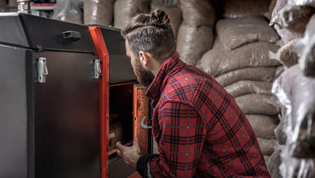 A man in a room with a solid fuel boiler, working on biofuel, economical heating.の写真素材