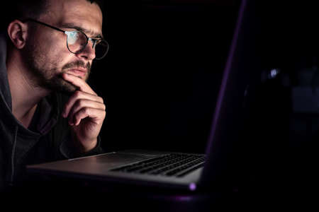 A man with glasses in the dark looks at the computer screen, copy space.の写真素材