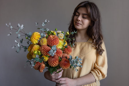 Attractive young woman in a yellow dress with a bouquet of bright chrysanthemums on a gray...