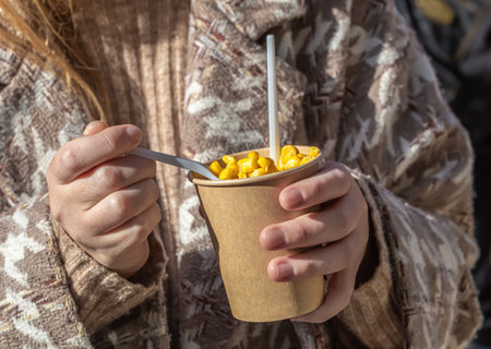 Boiled corn in a glass. Corn in the park. A woman is eating corn on a walk in the park. Snack on a walk.の写真素材