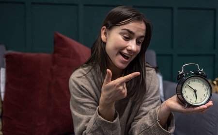 Black retro alarm clock in female hands on a blurred background.