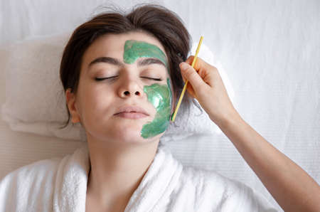 The process of applying a green cosmetic mask to the face of a young woman.の写真素材