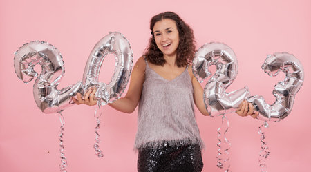 Cheerful girl with silver foil balloons in the form of numbers 2023.