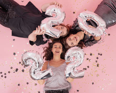 Cheerful girls lie on pink background with silver balloons 2022, top view.の写真素材