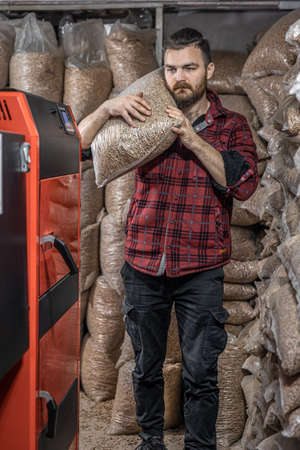 The man loads the pellets in the solid fuel boiler, working with biofuels.の写真素材