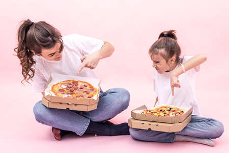 Funny girls with pizza in boxes for delivery on a pink background.の写真素材