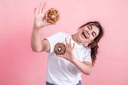 Portrait of a pretty, young woman showing donuts isolated over pink background.