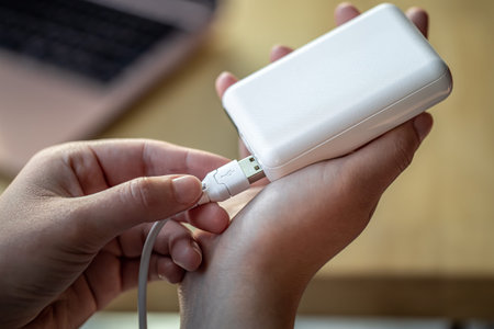 Womans hand holding white USB cable and white power bank.