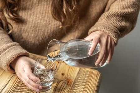 A woman pours water into a glass from a glass decanter.の写真素材