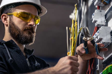 A male electrician works in a switchboard with an electrical connecting cable.の写真素材