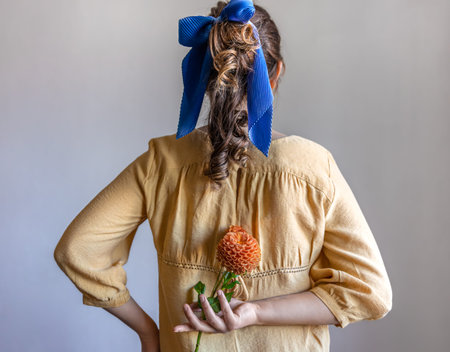 Back view, a girl holds a chrysanthemum flower behind her back, gray background.