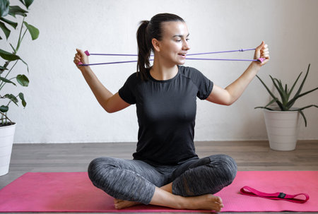 Young woman doing exercises with a fitness elastic band at home.