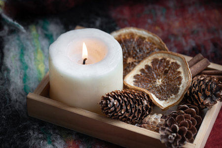 Close-up of a burning candle, pine cones, dried oranges and cinnamon.