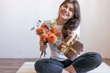 Young woman with a gift box and a bouquet of chrysanthemum flowers.の写真素材
