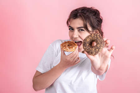 Portrait of a pretty, young woman showing donuts isolated over pink background.の写真素材