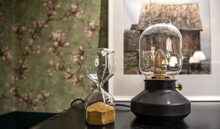 Close up of glass hourglass and vintage lamp in the interior of the room.