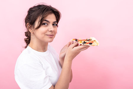 Attractive girl with a piece of pizza on a pink background, copy space.