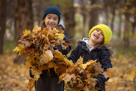 Two little girls are playing in the autumn leaves for a walk in the forest.
