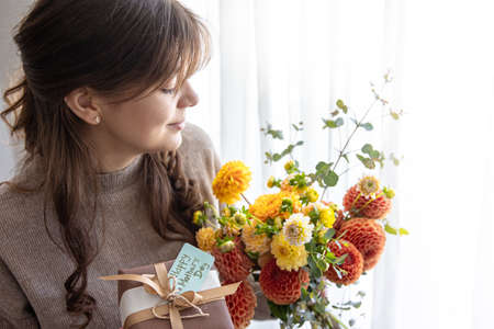 Young woman with a gift for mothers day and a bouquet of flowers in her hands.の写真素材