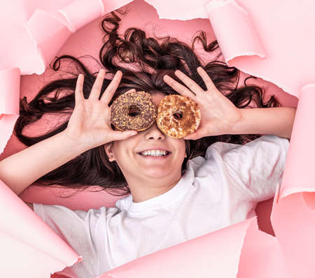 Cheerful girl with bright donuts on a paper pink background.の写真素材