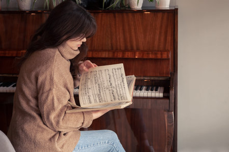 Young woman musician looks into a collection of notes, sitting at the piano.