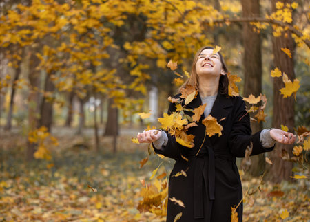 Happy young woman in the forest among autumn leaves on a blurred background.