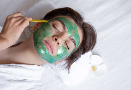 The process of applying a green cosmetic mask to the face of a young woman.の写真素材