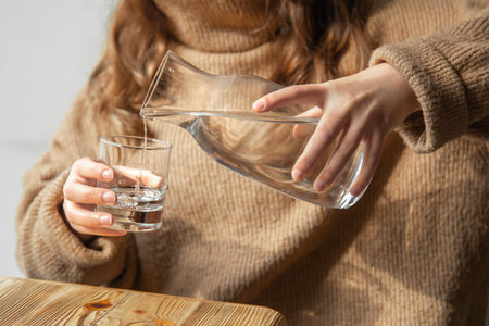 A woman pours water into a glass from a glass decanter.