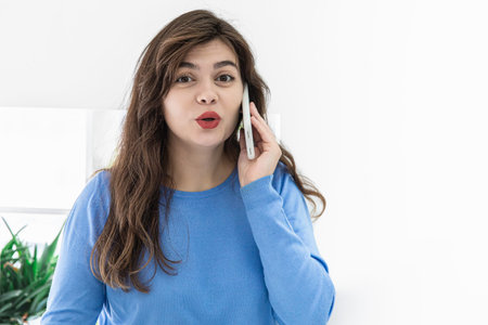Attractive young woman talking on the phone in a white interior, copy space.
