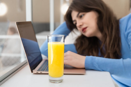 Attractive young woman with a glass of juice sits in front of a laptop.