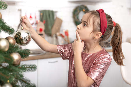 A little girl decorates a Christmas tree, hangs balls.の写真素材