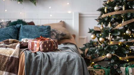 Interior of a cozy room with a Christmas tree and a gift box on the bed.の写真素材