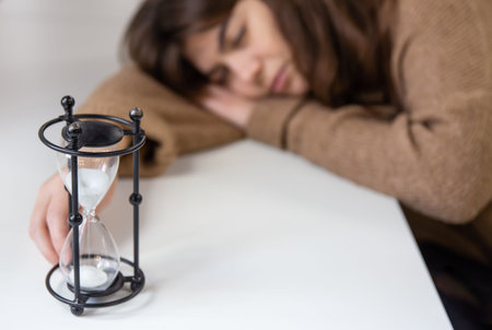 Vintage hourglass and sleepy young woman on blurred background.