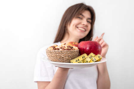 A plate with apples, nuts and a measuring tape in the hands of a young woman.の写真素材
