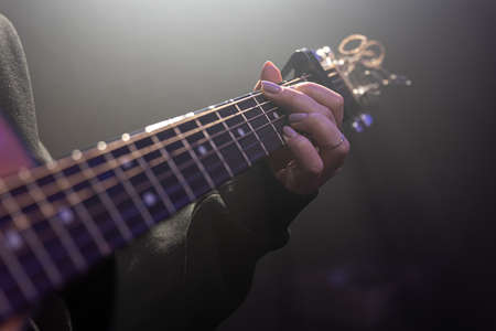 Close-up of female hands playing acoustic guitar in the dark.の写真素材